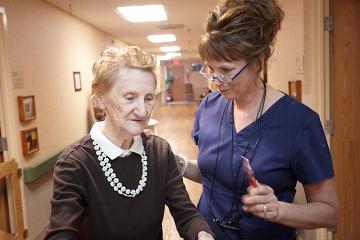 A nurse assisting an older woman down the hallway