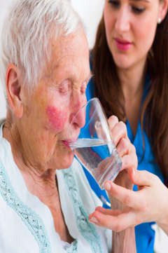 nurse helping an elderly woman drink water
