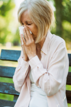 older woman sneezing at the park 