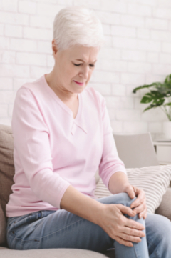 older woman holding her knee in pain on the couch 